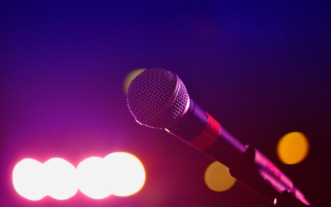 Close-up of a microphone on stage with colorful lights and a blurred background, capturing the vibrant energy of pop culture performances.