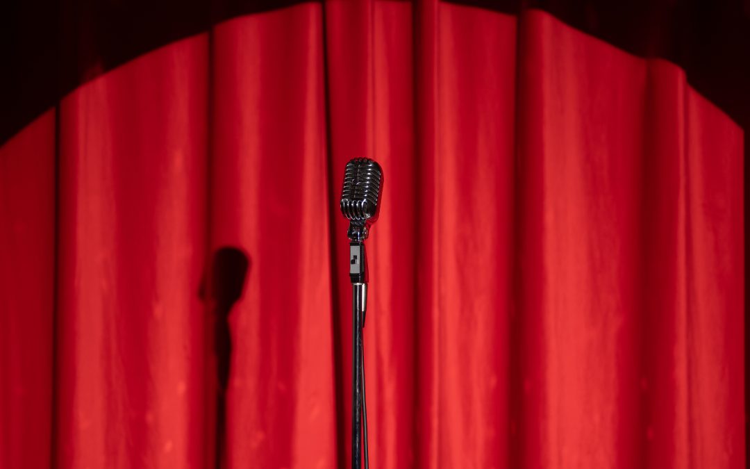 A vintage microphone on a stand in front of closed red stage curtains, perfect for adding a touch of classic elegance to corporate events.