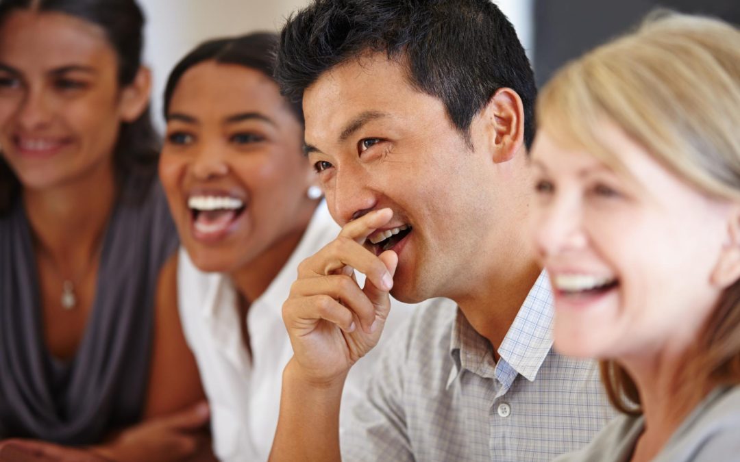 Four people sitting closely together, smiling and laughing in a bright indoor setting.